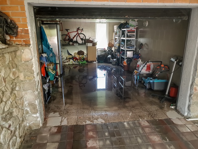 A flooded garage with lawn equipment and tools submerged in water