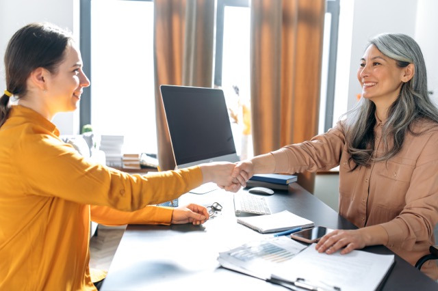 A customer and insurance agent shaking hands over a desk.